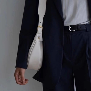 Detail of white leather crescent bag with gold hardware worn on navy blue blazer