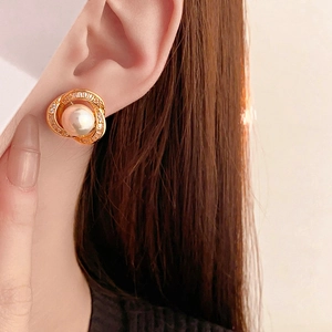 Dettaglio di orecchini d'oro con perla bianca e intarsio di zirconi sull'orecchio della modella