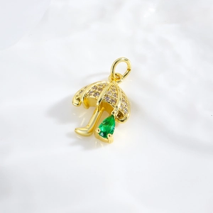 Dettaglio di un ciondolo a ombrello dorato con zirconi e una pietra preziosa verde