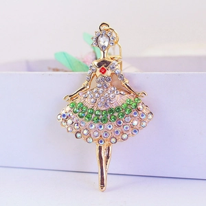 Porte-clés ballerine dorée avec strass verts et transparents sur un fond de boîte blanche