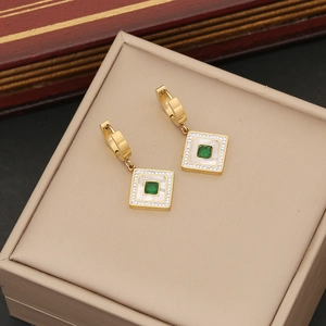 Detail of golden huggie hoop earrings with emerald square stone and mother of pearl