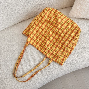 Vue détaillée du cabas en toile à carreaux jaune et orange sur un canapé blanc