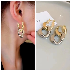 Detail of interlocking gold and silver dual-tone oval hoop earrings on model and table
