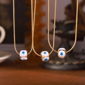 Goldene Schlangenkette mit weißem Evil Eye Emaille-Anhänger vor warmem Hintergrund