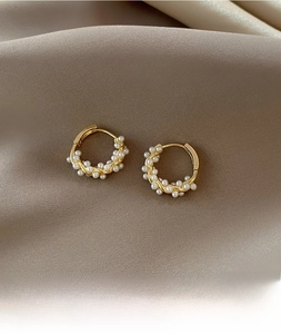 Detail of twisted gold hoop earrings with white pearls on a silk background