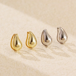 Macro shot of minimalist gold and silver water drop earrings on a textured stone surface
