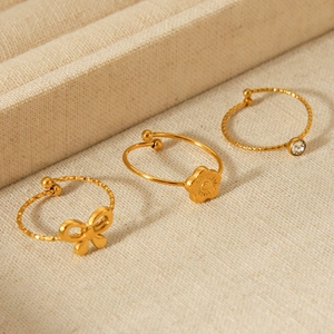 Detail of 18K gold plated bow and flower rings set with zircon on beige fabric