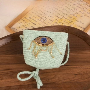 Detailed view of the light green woven straw bag with a rhinestone eye design on a tray
