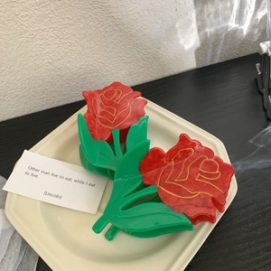 Large red rose hair claw clips with green leaves made of glossy acetate in ceramic tray