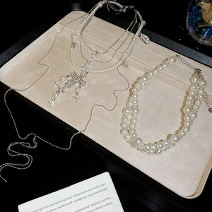 Detail of layered pearl necklaces with diamond cross pendant on a beige jewelry tray