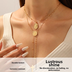 Close-up of layered gold necklace featuring a cross relief pendant and a round coin medallion