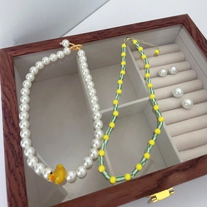 Charming beaded necklaces with yellow duck pendant and pearls in a wooden jewelry box
