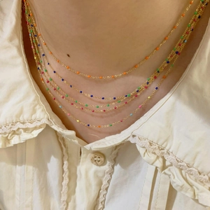 Gros plan d'un collier doré à cinq rangs avec perles colorées sur chemise en dentelle