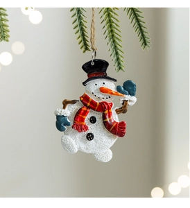 Close-up of resin snowman ornament with red scarf hanging on a pine tree branch