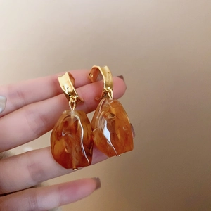 Detail shot of irregular amber resin earrings with gold metal hoops on hand