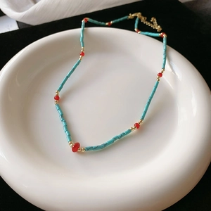 Close-up of bohemian turquoise beaded necklace with red and gold accents on white tray