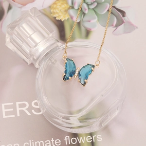 Detailed view of a gold butterfly necklace with blue crystals on a perfume bottle