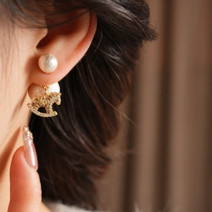 Close-up of a zircon rocking horse earring with a pearl drop on a model's ear