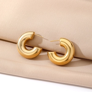 Macro shot of gold chunky C-shaped hoop earrings with mirror polish on beige satin