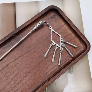 Detail of silver tassel hair pin with hollow tower design on a rustic wooden tray