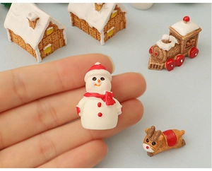 Close-up of a tiny resin snowman with a red scarf held on a finger for scale