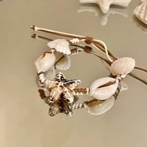 Macro detail of handmade starfish seashell bracelet on a golden reflective mirror background