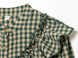 Detail of green plaid shirt with ruffled shoulders and wooden buttons on the neckline