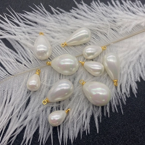 Teardrop imitation pearl pendants with gold rings on white feathers and black background