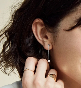 Detail view of model wearing gold tassel earrings and an engraved initial ring