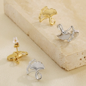 Macro view of gold and silver stainless steel ginkgo leaf stud earrings on stone