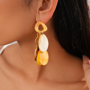 Macro detail of long acrylic geometric drop earrings with amber and cream resin pendants