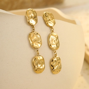 Golden geometric dangling earrings with hammered texture on white ceramic stand