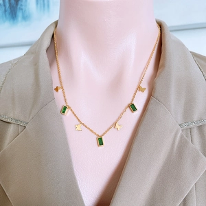 Elegant gold butterfly necklace with green rectangular gemstones on a model in a beige blazer