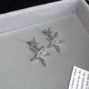 Detailed view of silver star earrings with clear zircon stones on a grey velvet tray