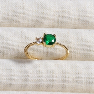 Macro shot of 18K gold rope ring featuring round green emerald and clear side stones