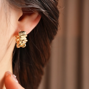 Close-up of golden huggie hoop earring with irregular crumpled texture on ear