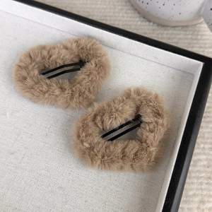 Detail of two beige fuzzy heart hair clips with soft plush texture on linen tray