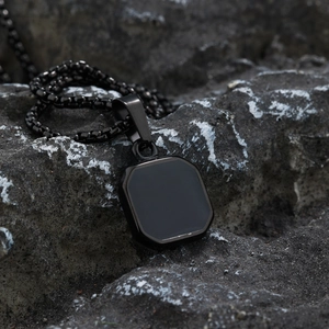 Men's black stainless steel square pendant necklace on a rugged volcanic rock background