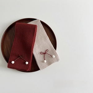 Detail of red and cream knit scarves with bowknot and pompons on a wooden tray