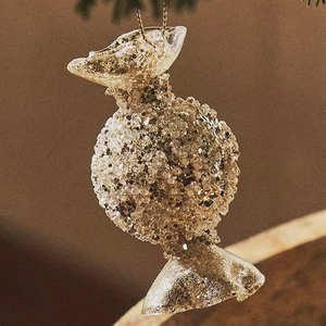 Champagne candy-shaped glass Christmas ornament with gold glitter hanging on a tree