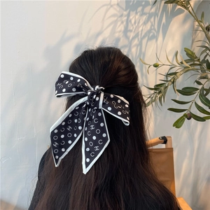 Dettaglio di un nastro per capelli in seta a pois bianchi e neri annodato a fiocco