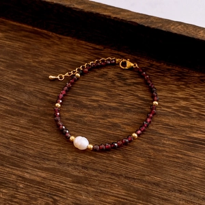 Detail of beaded necklace featuring red faceted stones, a central baroque pearl and gold accents