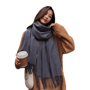 Model wearing a thick grey cashmere scarf with tassels and brown knit sweater