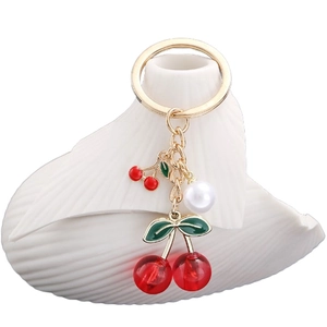Golden keychain featuring red cherry pendants and white pearl on a shell tray