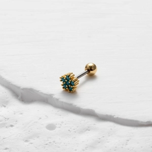 Macro detail of gold barbell stud earring with turquoise stone cluster on stone surface
