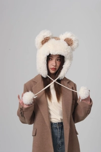 Detail of cream plush earflap hat with brown bear ears and fluffy pom-pom ties