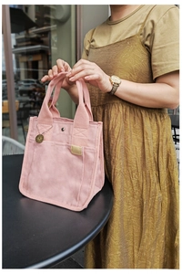 Detailstruktur der rosa Canvas-Handtasche mit Metall-R-Anhänger auf einem Tisch