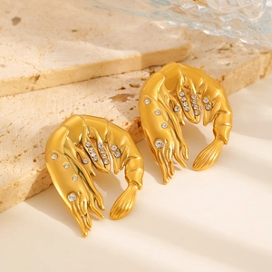 Vue détaillée de boucles d'oreilles homard dorées avec zircons sur un support en pierre