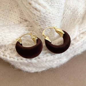Detailed close-up of dark brown velvet hoop earrings on a beige knit sweater background