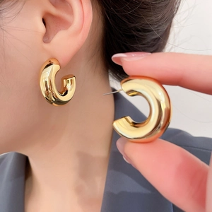 Close-up of chunky C-shaped gold polished hoop earrings in minimalist French style